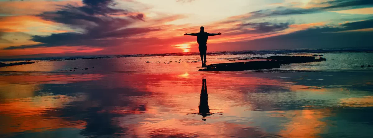 Person with their arms outstretched looking at a vivid sunset