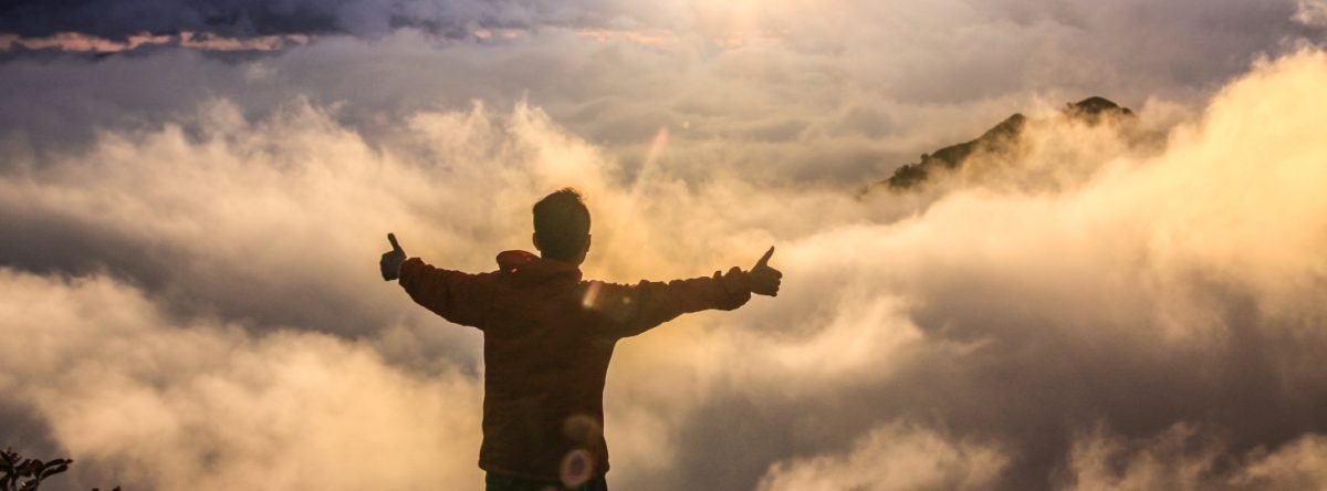 A man stands with arms raised at the top of a mountain as the sun rises