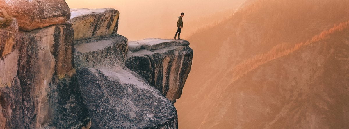 A person peers over a precipitous cliff edge